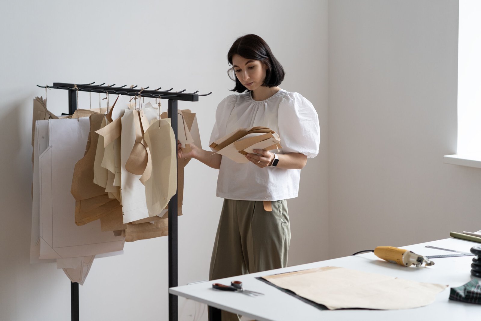 Dressmaker girl looking at patterns drafts for clothes in atelier. Fashion designer inspiring for work. Young female successful small tailor business owner or employed seamstress in workshop studio