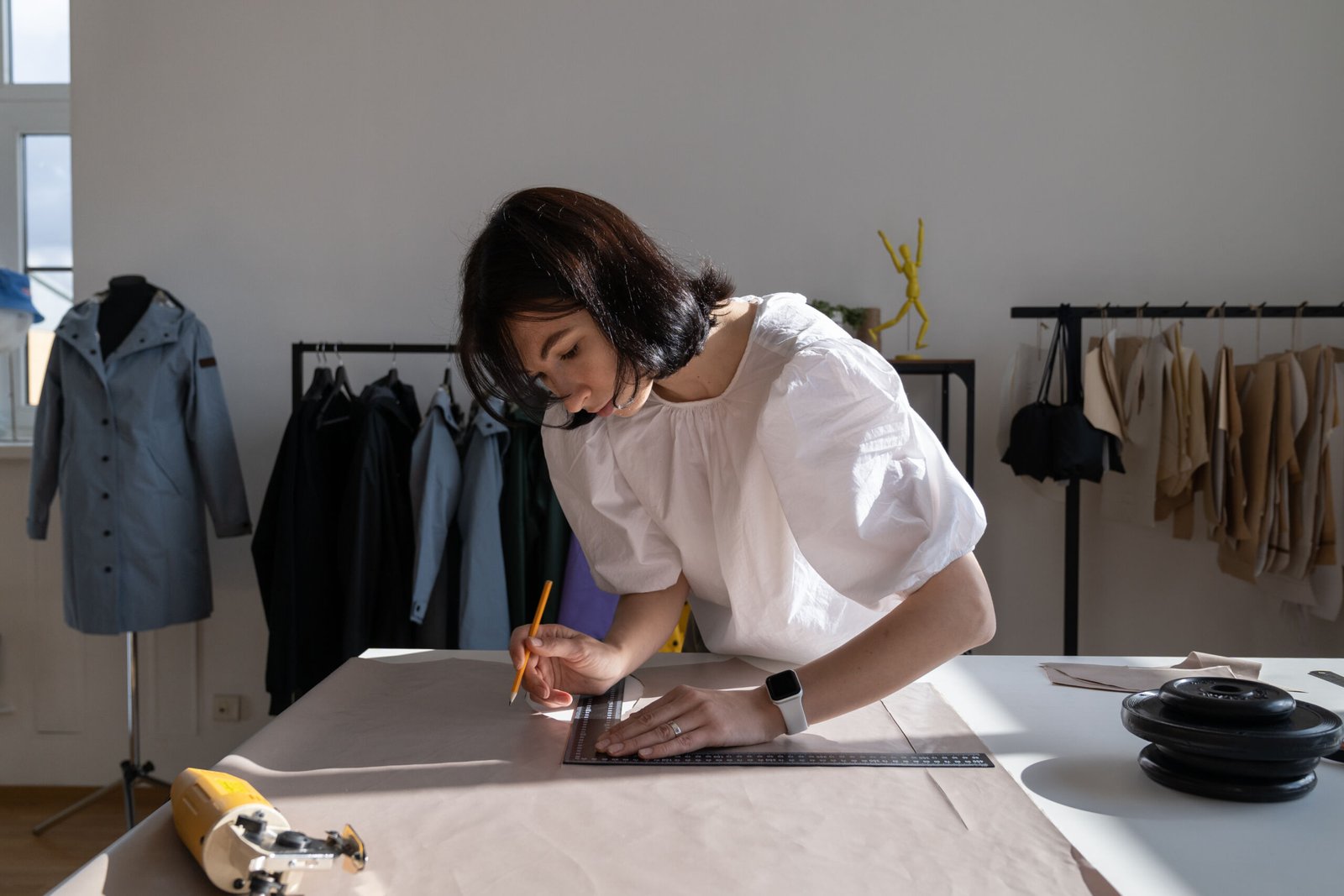 Tailor work with cloth in atelier. Young woman designer measure material with plastic ruler on dressmaking table in creative design workshop. Female fashion studio owner busy with garment tailoring